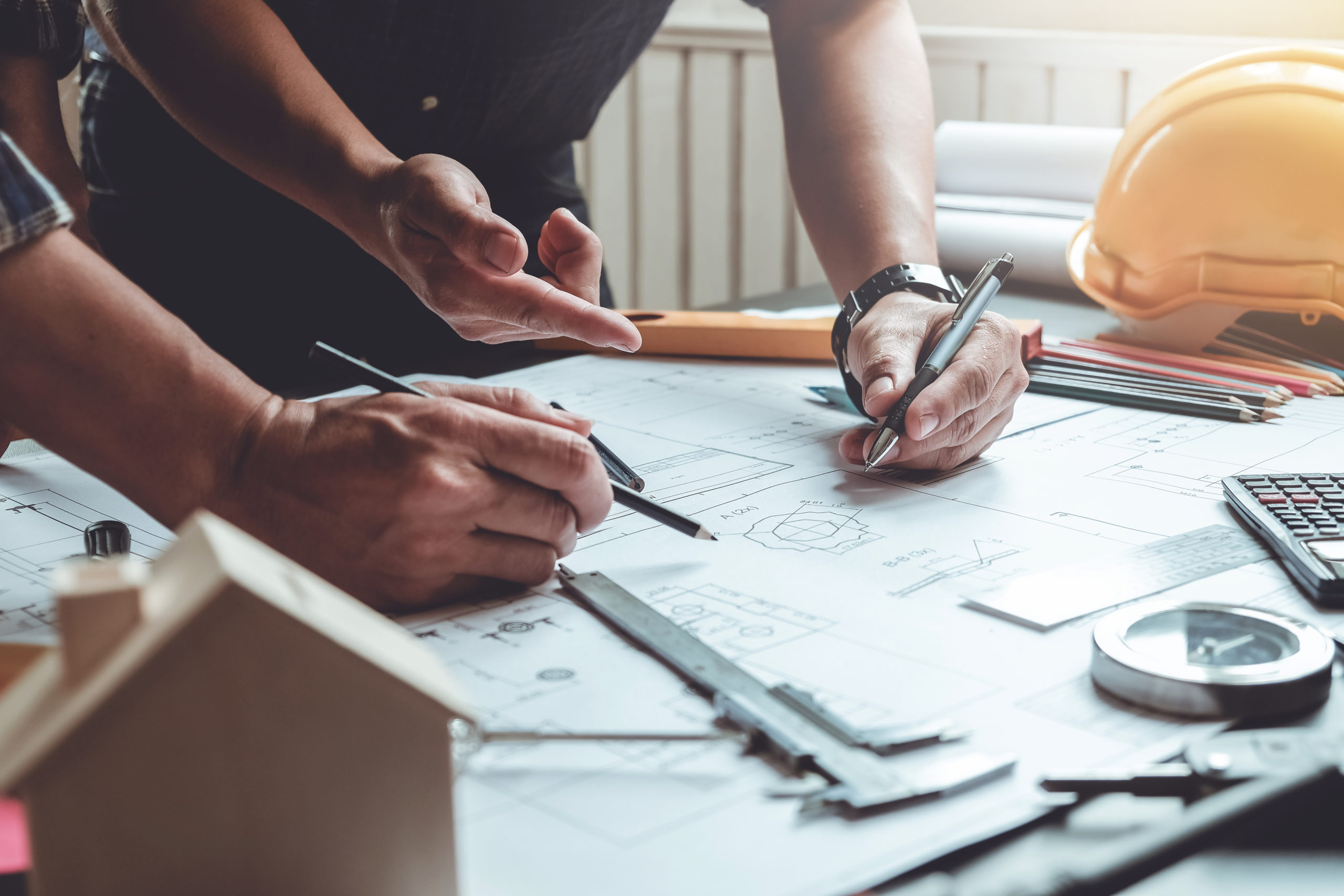 Two architects planning together at desk with blueprints.