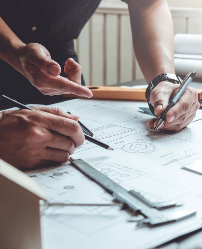 Two architects planning together at desk with blueprints.
